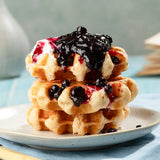 Stack of waffles with jam on a plate against a light blue background