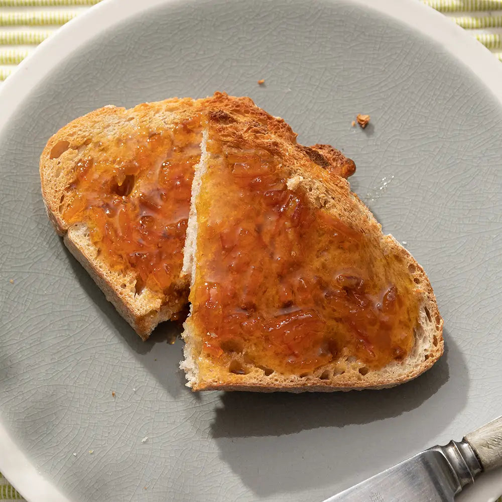 Two slices of toast with marmalade on a grey plate with a knife.
