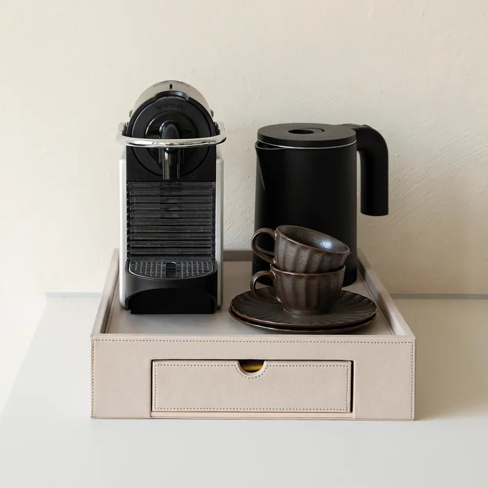 Coffee machine, black kettle, and cups on a beige tray with a drawer.