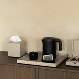 Black electric kettle on a tray surface with a tissue box and other items.