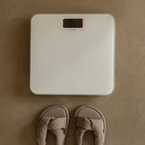 White digital bathroom scale on a brown surface with beige sandals in front