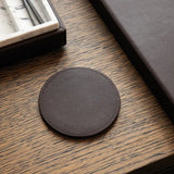 Round dark brown leather-effect coaster on a wooden surface