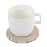 White ceramic mug on a beige leather-effect coaster with a white background