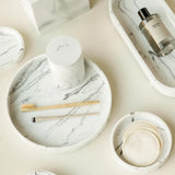 Marble-patterned amenity trays, a Toba jar and a brush on a light surface.