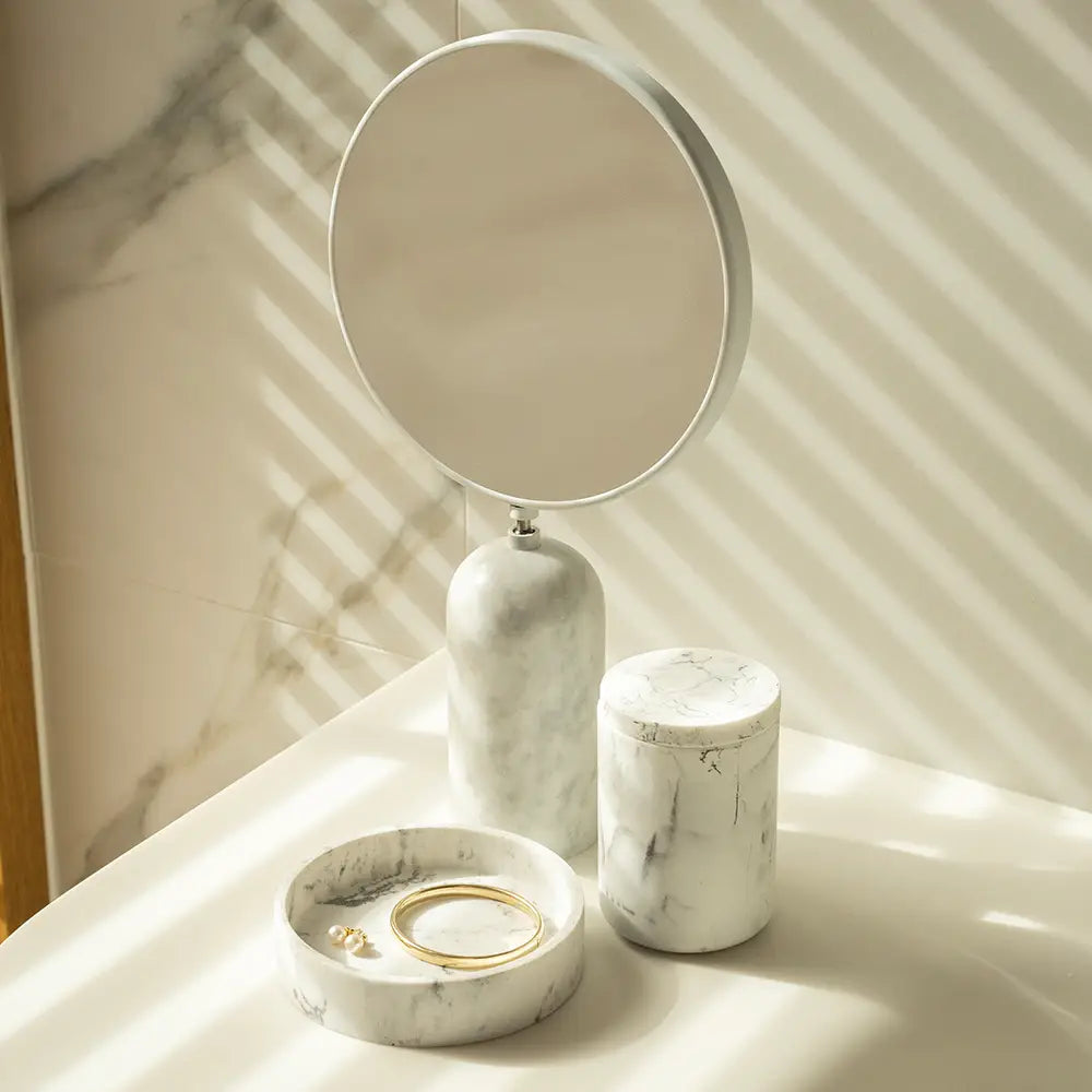 Marble-textured vanity set with round mirror, cylindrical container, and jewelry dish on a marble surface.