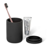 Black amenity jar with a toothbrush, black lid, and toothpaste on a white background