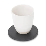 White ceramic cup on a black leather-effect coaster against a white background
