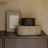 Two leather-effect boxes, one beige and one black, on a wooden surface with a framed picture in the background