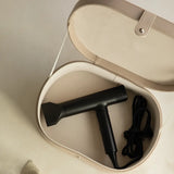 Black hair dryer in a beige storage case on a light brown surface
