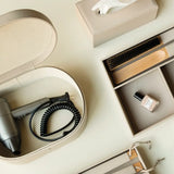 Travel-sized hair dryer in a beige storage case with tissues, and nail polish on a light surface.