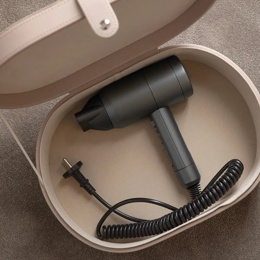 Black hair dryer with coiled cord inside a beige storage case