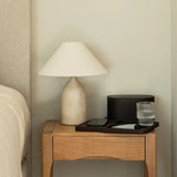 Nighstand with lamp, glass, and phone against a neutral wall