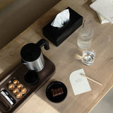 Wooden table with coffee-making items on a brown tray, a glass of water, and a tissue box