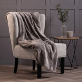 Blanket draped over a chair with a side table and a plant in the background.