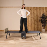 Woman standing on a bed in a room with wooden flooring and a plant.