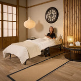 Woman sitting on a bed in a room with wooden walls and a large clock.
