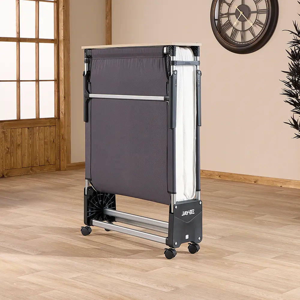 Portable folding bed on wheels in a room with wooden floor and clock on wall.