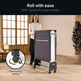 Woman pushing a folding bed with 360° castors in a room with wooden flooring and large windows.