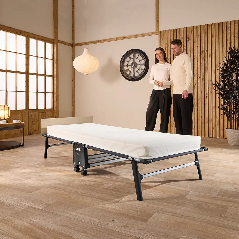 Two people standing in a room with a bed on the floor.