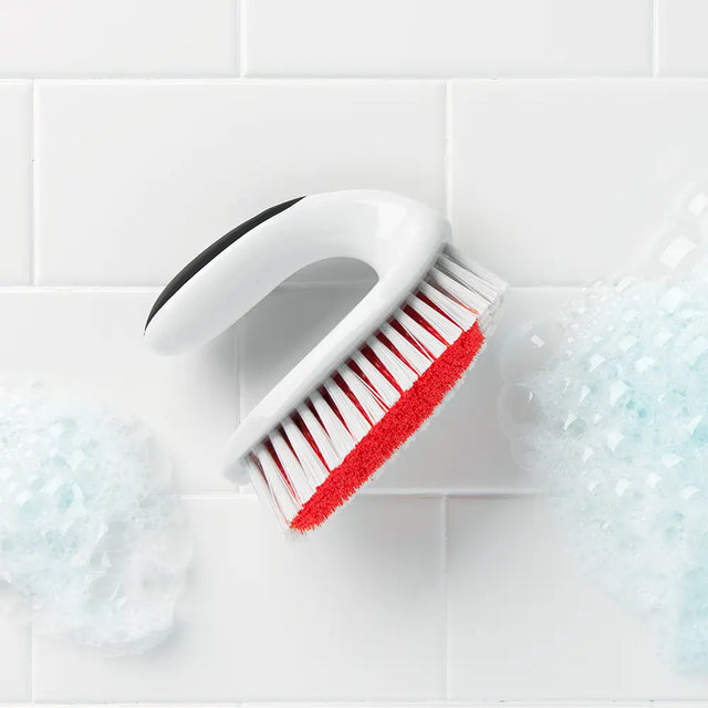 Scrubbing brush with red bristles on soapy tiled surface, cleaning products