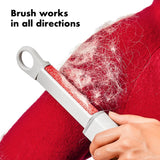 Person using a pet hair removal brush on a red fabric with text 'Brush works in all directions'.