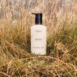 A bottle of Scottish Fine Soaps 'Au Lait' hand and body lotion, featuring a matte white bottle and a black pump dispenser, in a grassy field