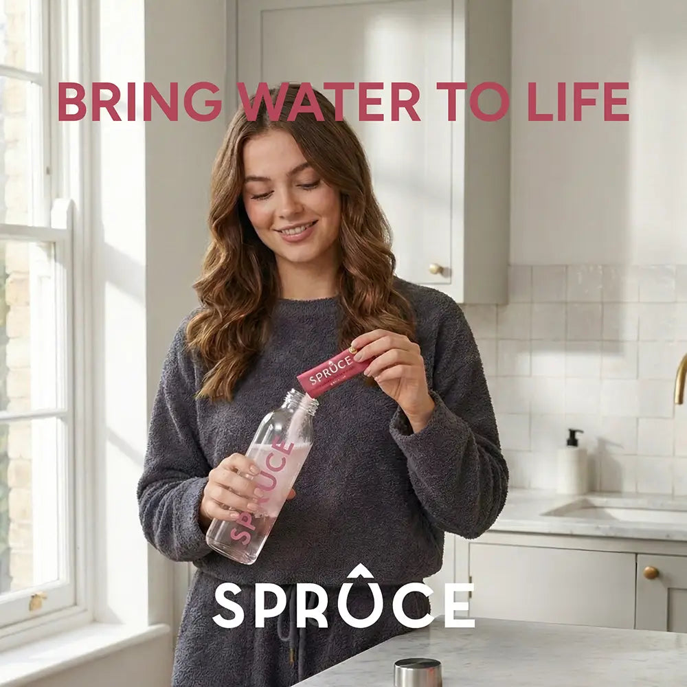 Woman pouring a Spruce Raspberry & Elderflower sachet into a Spruce water bottle in a kitchen, 'Bring Water To Life' tagline