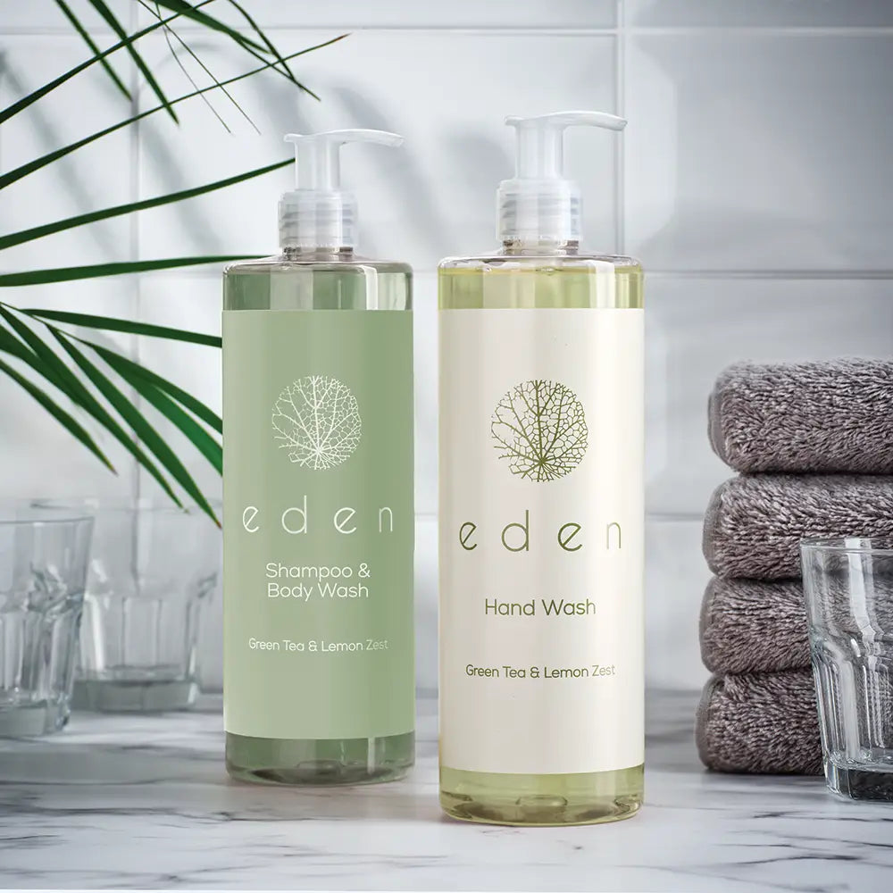 Two bottles of Eden green tea and lemon zest Shampoo & Body Wash and Hand Wash 500ml on a bathroom counter with towels and glasses in the background.