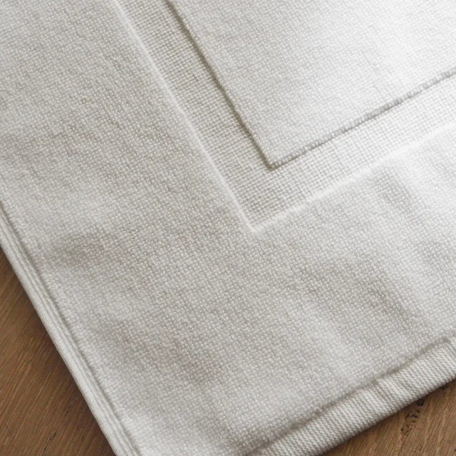 Corner of white luxury 900gsm cotton pedestal mat designed to fit around the base of a toilet.