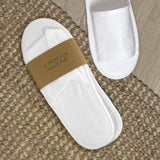 White slippers with a brown band labeled 'A Treat for Your Feet' on a textured surface.