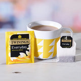 Twinings everyday tea package, cup, and tea bag on a light surface with a blurred colorful background
