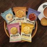 Assorted packages of Border cookies on a wooden surface with a cup of tea.