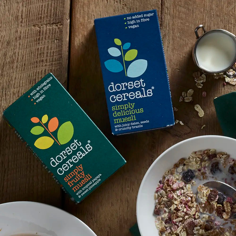 Two boxes of Dorset Cereals on a wooden table with a bowl of cereal.