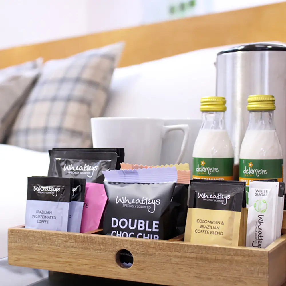 Assorted coffee products including bags and bottles on a wooden tray in a hotel setting