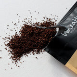 Open black coffee bag spilling coffee grounds on a white surface