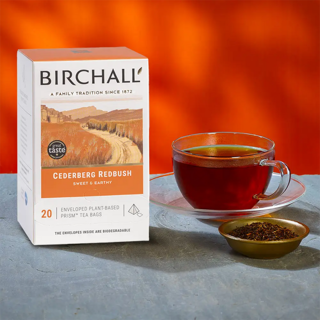 A box of 20 Birchall Redbush Tea Bags next to a cup of brewed tea and ramekin of reddish tea leaves