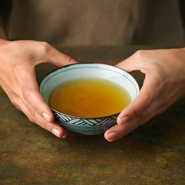 Mao Feng Green Tea brewed in a small bowl held by two hands