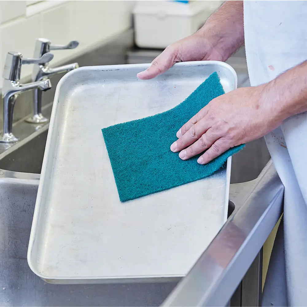 Person cleaning a metal tray with a green scourer 
