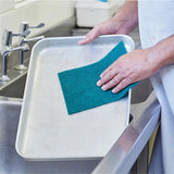 Person cleaning a metal tray with a green scourer 