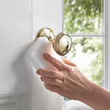 Magic sponge cleaning a gold doorknob on a white door, blurred greenery outside