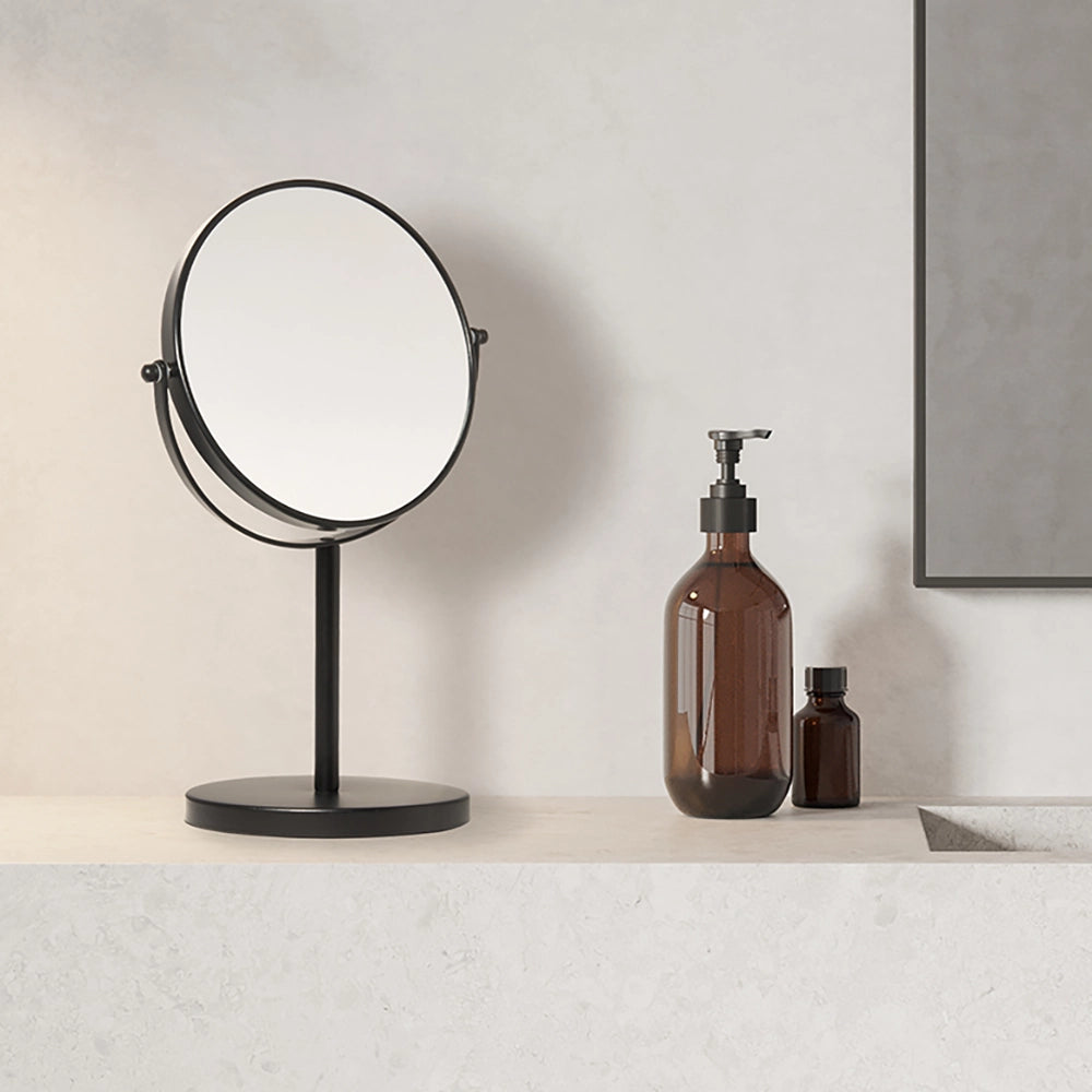 Black vanity mirror on a white countertop with brown bottles against a neutral wall.