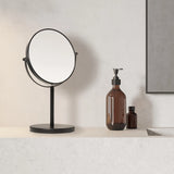 Black vanity mirror on a white countertop with brown bottles against a neutral wall.