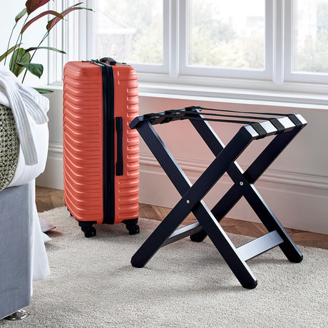 Black wood luggage stand with suitcase by the side in a bedroom setting