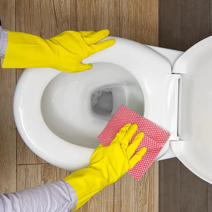 Person wearing yellow rubber gloves cleaning a toilet with a red cloth