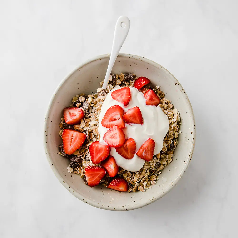 Bowl of Dorset Cereals Simply Delicious Muesli Portion Packs with yogurt and strawberries on a white background